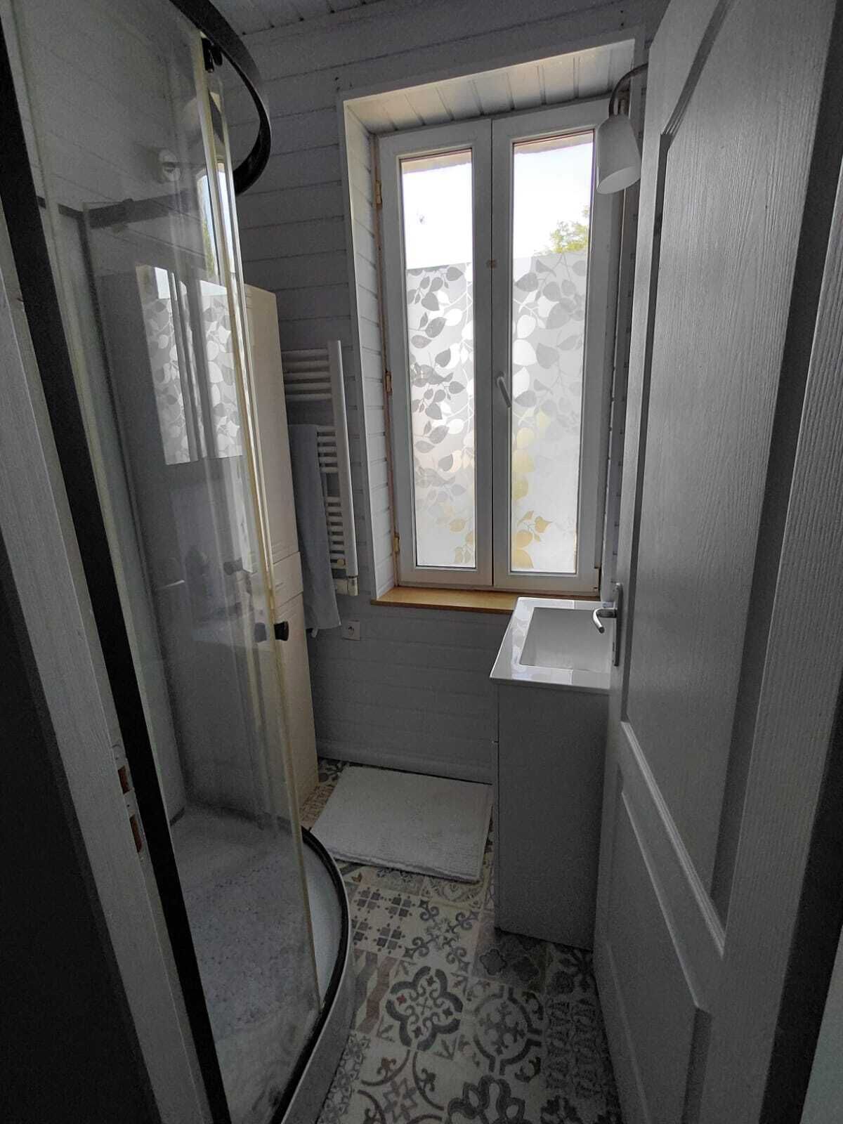 Een kleine badkamer met een raam, een handdoekhouder en een wastafel.
