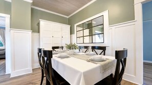 A dining room with a white table set for four, flanked by dark wooden chairs, against a green wall with white trim. - Charming 3BR Farmhouse, Near Trails & Town (Fruita)