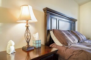 Un lit bien fait, avec une tête de lit sombre, une lampe de chevet, une boîte de mouchoirs et une petite figurine blanche posée sur une table de chevet en bois.