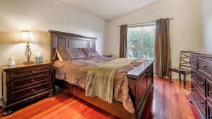 A bedroom with a wooden bed, a nightstand, a dresser, and a window with curtains.
