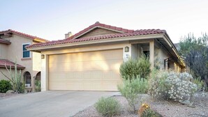 A single-story house with a beige garage door, a red-tiled roof, and a small porch with a railing.