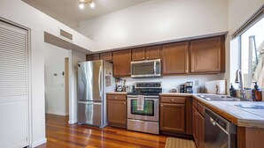 A modern kitchen with stainless steel appliances, wooden cabinets, and a large window providing natural light.