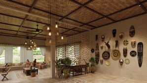 A spacious room with a high ceiling, woven ceiling, and hanging lights. There are several wooden tables and chairs, and a large patterned rug on the floor. - Brij Sone Bagh, Bandhavgarh | A Luxury Jungle Retreat (Umaria)