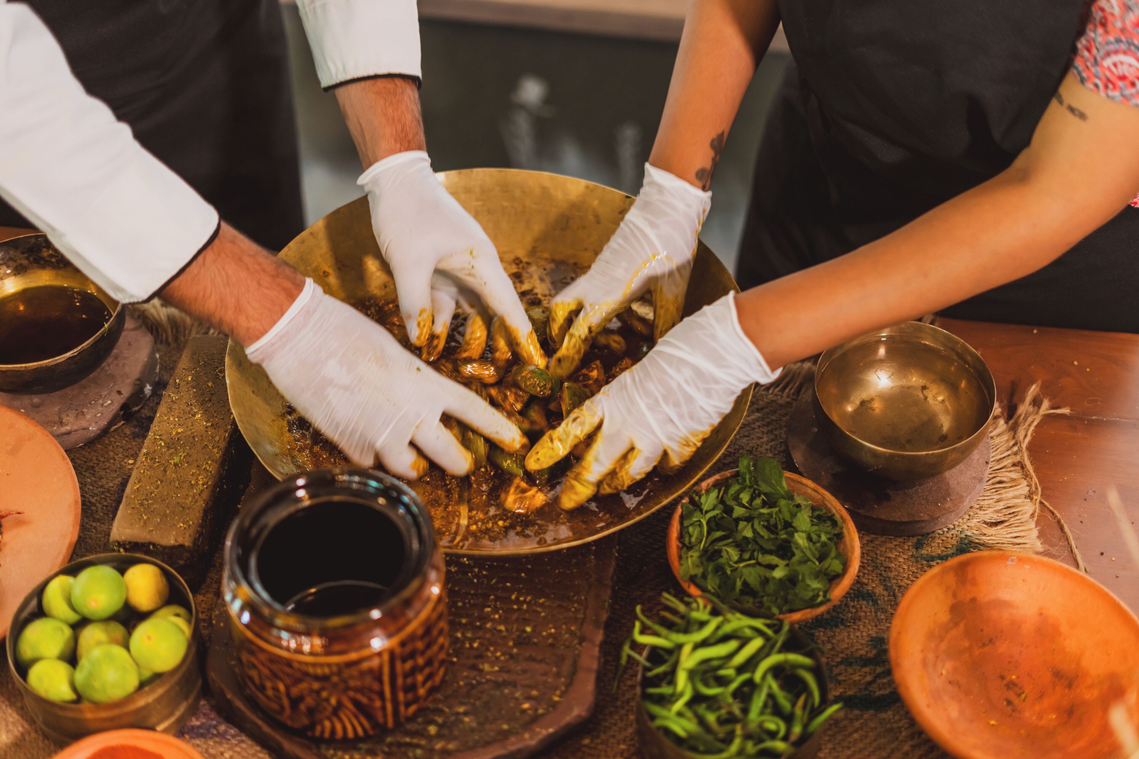 A group of people wearing gloves handling food items in a kitchen setting.
