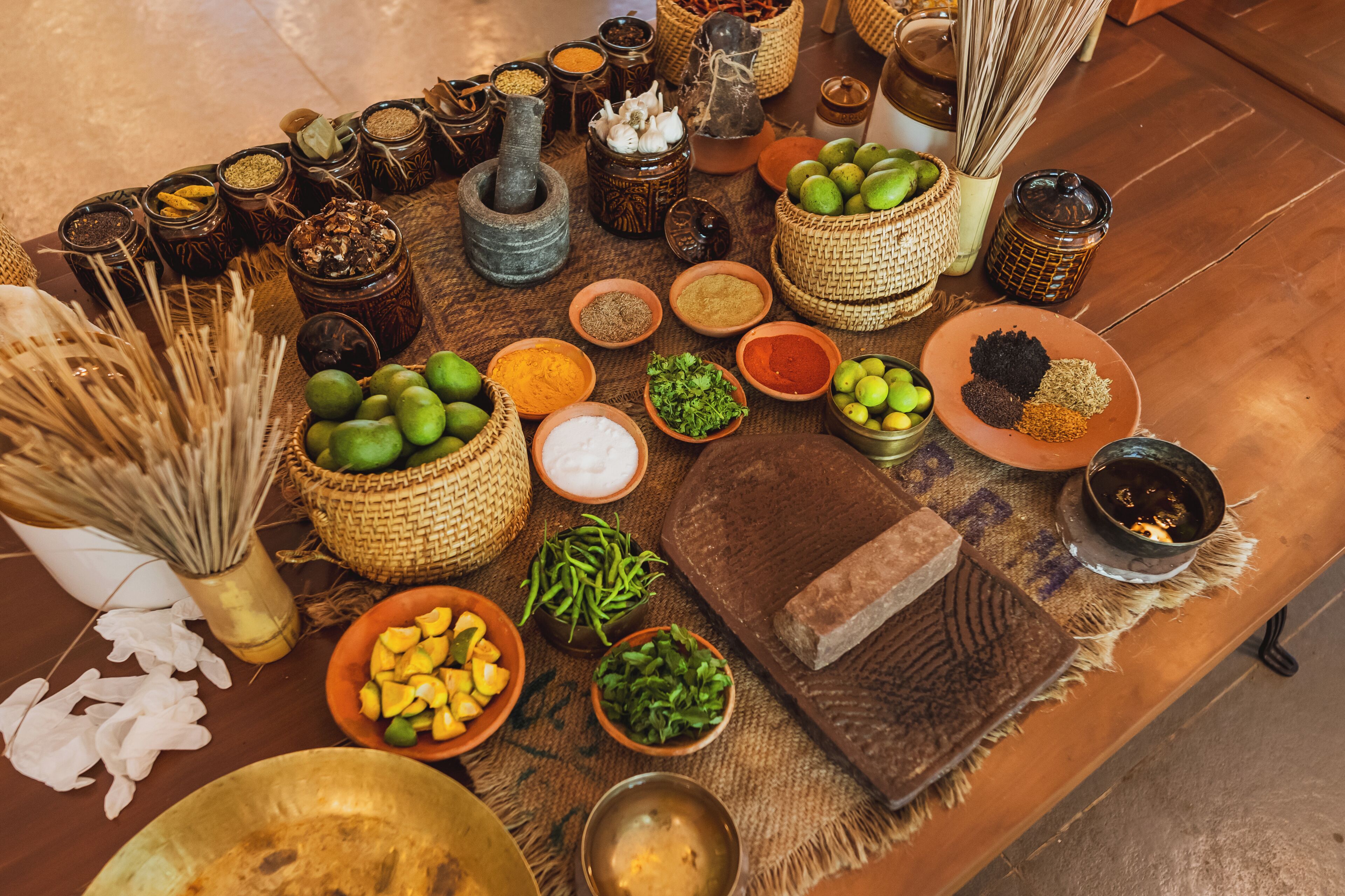 A variety of spices and herbs arranged on a woven mat, with some in ceramic containers and others in baskets.