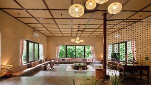 A spacious living area with a large window, a sofa, a coffee table, and potted plants. - Brij Sone Bagh, Bandhavgarh | A Luxury Jungle Retreat (Umaria)