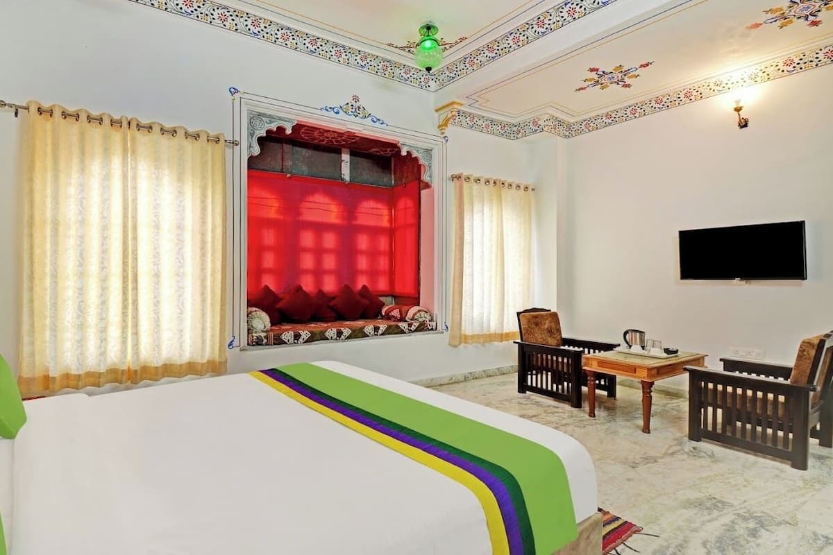 Une chambre d’hôtel avec un lit, une petite table avec des chaises, une télévision et une fenêtre avec des rideaux.