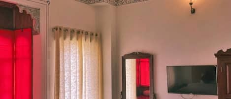 A room with a bed, a television, a mirror, and a window with curtains.