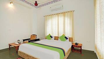 A hotel room with a bed, a nightstand, a chair, a table, and a window with curtains.