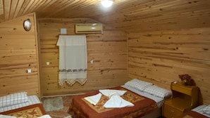 Un chalet confortable aux murs et au plafond en bois, comprenant trois lits avec une literie et des serviettes à motifs, une petite table de chevet en bois et un luminaire au plafond.
