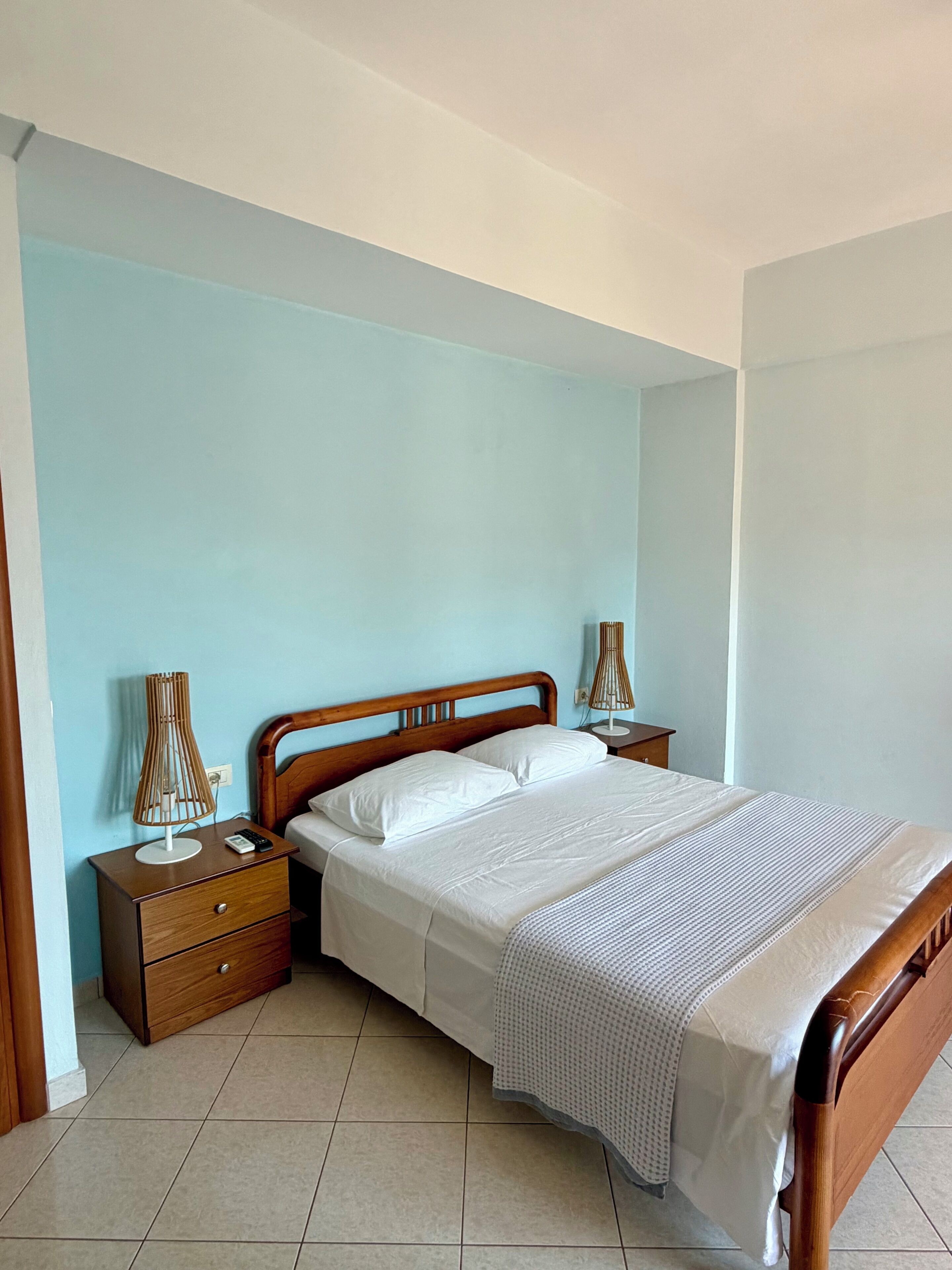 A neatly made bed with white linens, a wooden headboard, and a bedside table with a lamp.