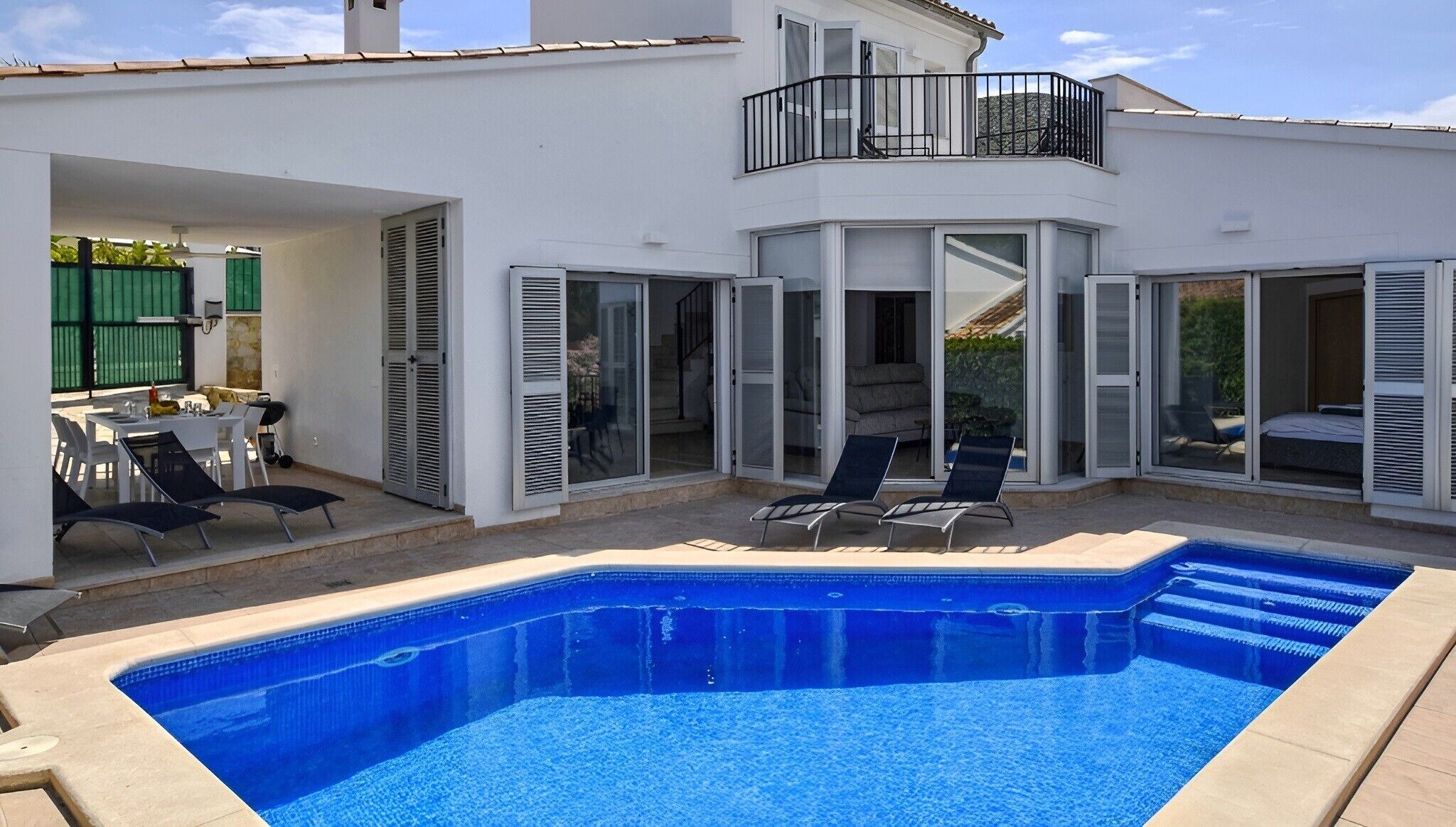 A swimming pool with a sun terrace, outdoor seating, and a covered patio area.