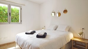 Ein Schlafzimmer mit einem Bett, Kissen, einem Nachttisch mit Lampe und einem Fenster mit Blick auf Grünflächen.