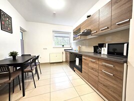 Una cocina moderna con armarios de madera, horno empotrado, microondas y comedor con mesa y sillas.