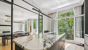 Una cocina moderna con encimera de mármol, ventanas amplias y una zona de comedor con mesa y sillas.