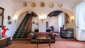 A spacious room with a grand staircase, a sofa, a table with a vase, and a dining area with a clock on the wall. - Cosy apartment in villa for 6 guests with WIFI, pool, A/C, TV and pets allowed (Peccioli)