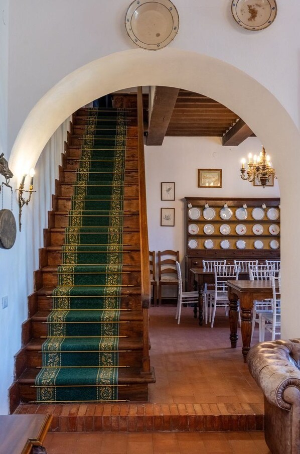Un escalier recouvert d’une moquette verte, avec des marches en bois et un lustre. On y trouve également un coin repas avec des chaises blanches et une table en bois.