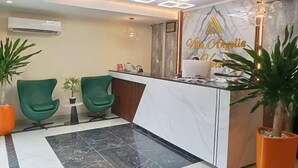 A reception area with a marble counter, two green chairs, and a modern ceiling light fixture. - Villa Angelia Hotel & Chinese Restaurant (Lagos)