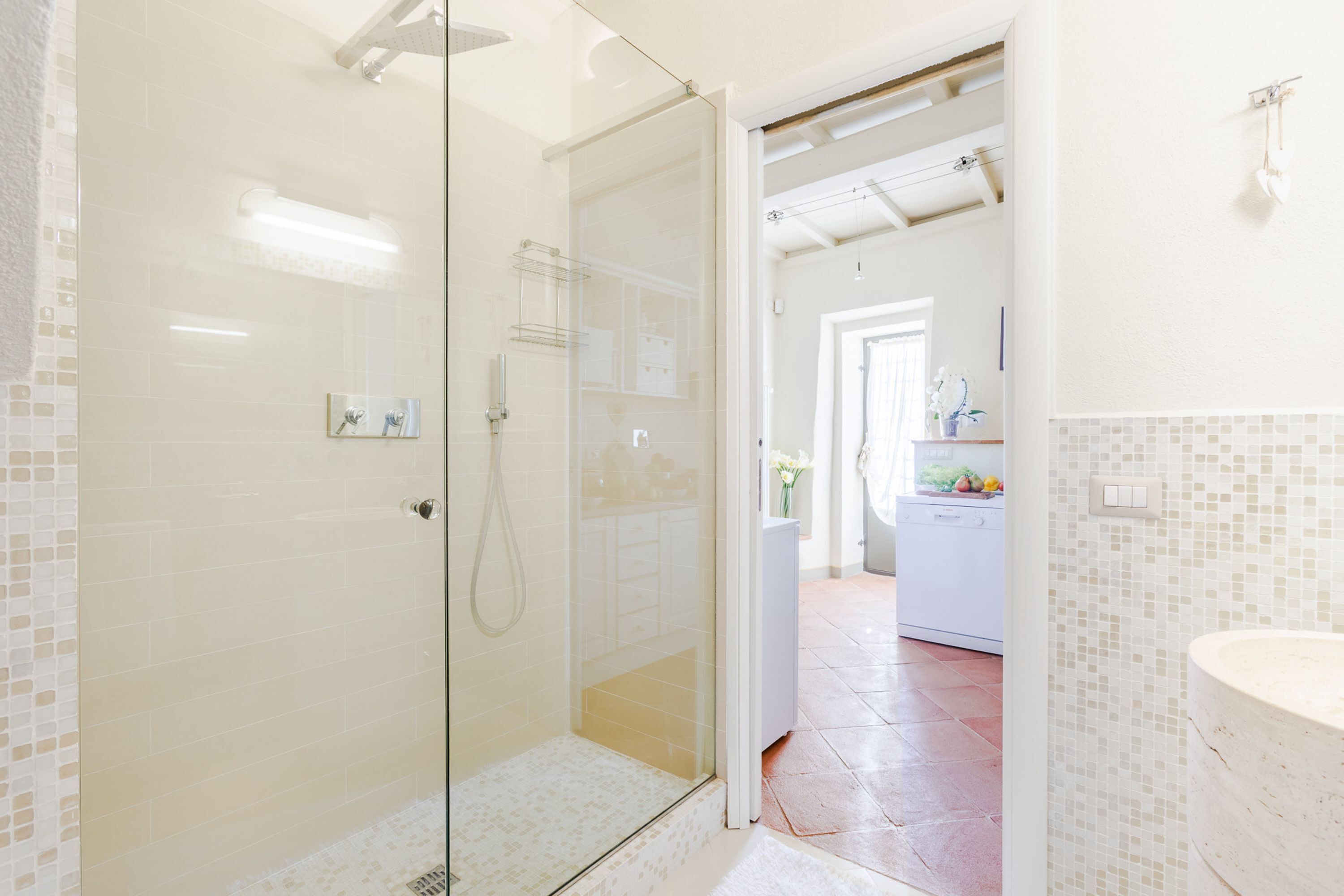 Ein modernes Badezimmer mit Duschkabine aus Glas, einem weißen Waschbecken und einem gefliesten Boden.