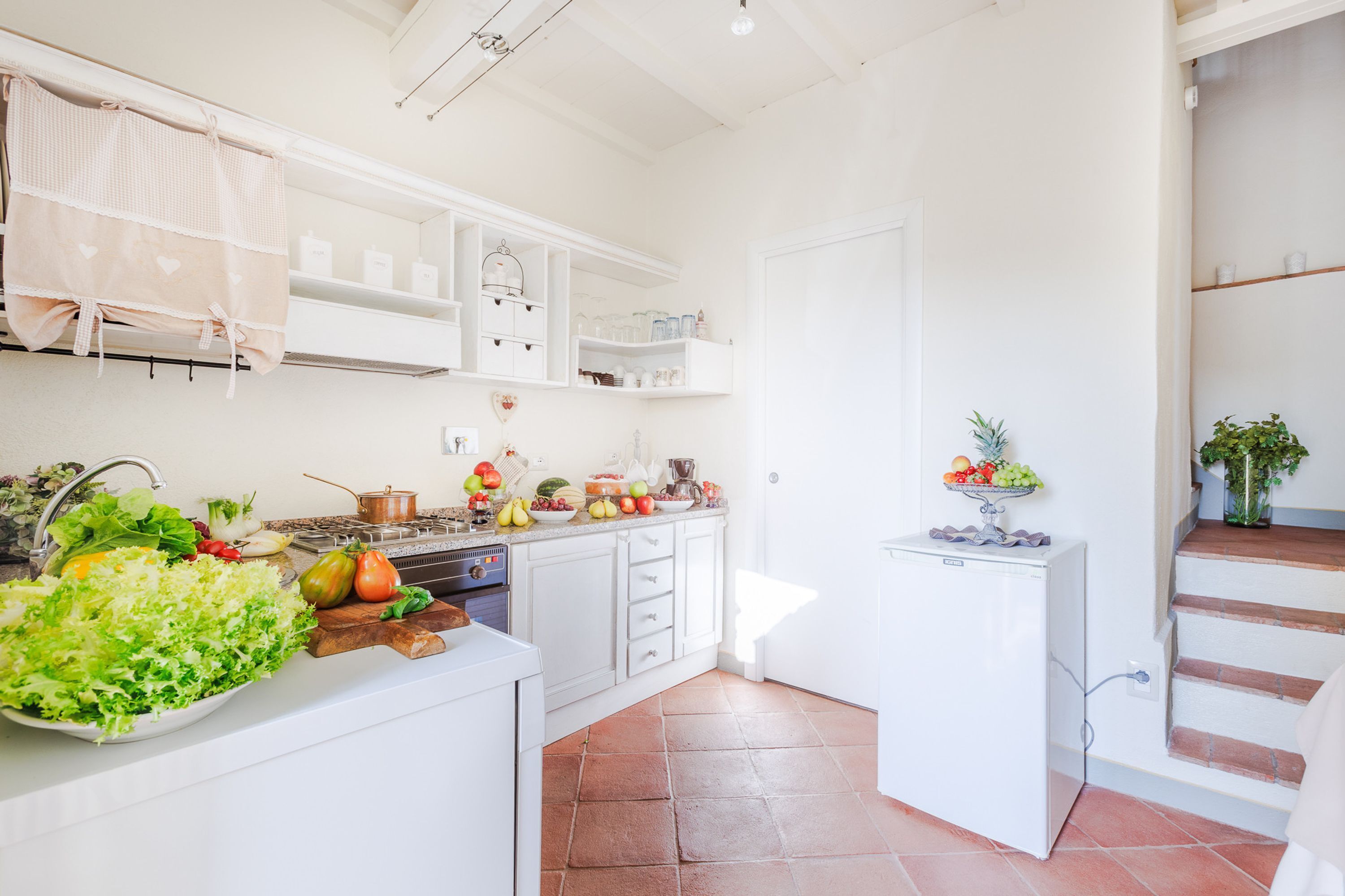 Een keuken met witte kastjes, een spoelbak en een aanrecht met vers fruit en groenten.