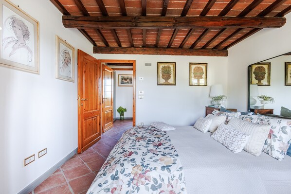 A bedroom with a bed, wooden ceiling beams, and framed artwork on the walls.