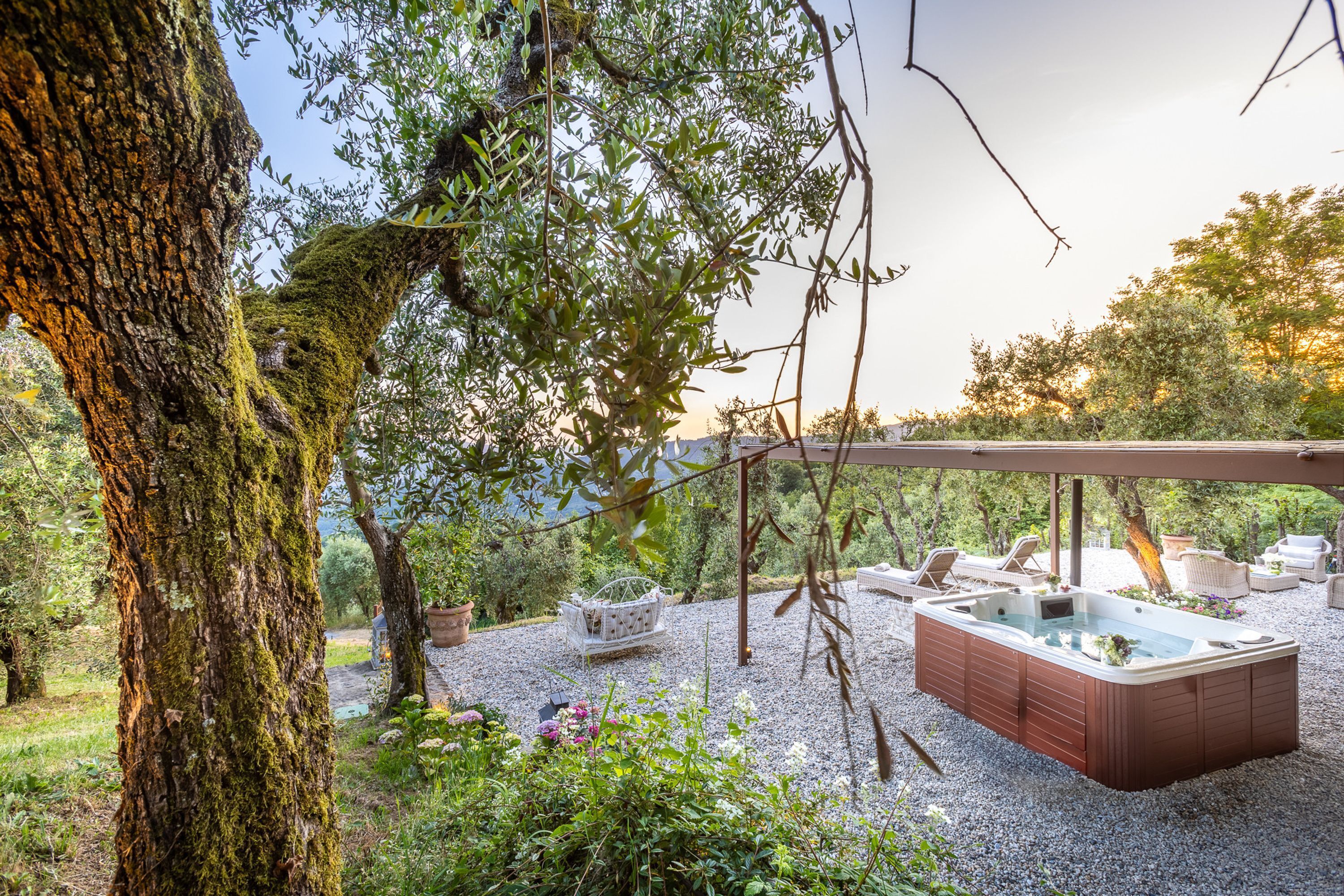 A hot tub under a pergola surrounded by outdoor furniture and greenery.
