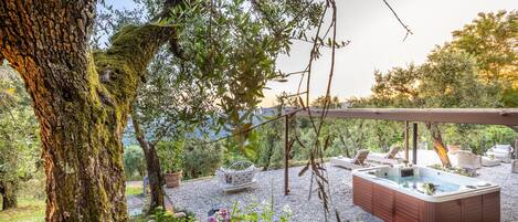 A hot tub under a pergola surrounded by outdoor furniture and greenery.