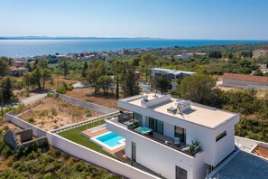 A modern villa with a swimming pool, a view of the sea, and a lush green landscape. - Villa Calvi Zadarvillas (Zadar)