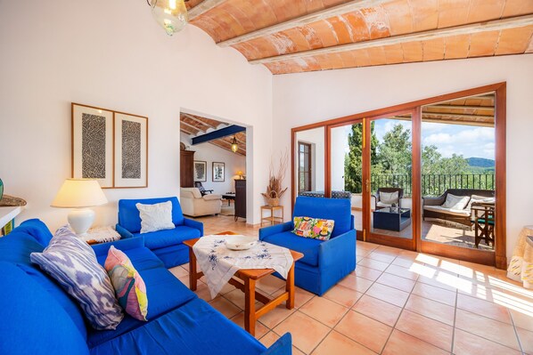 A spacious living area with blue sofas, a coffee table, and a view through a glass door to an outdoor seating area.