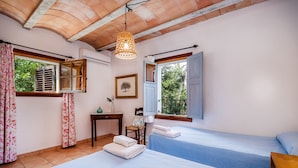 A room with two beds, a table, a chair, a hanging lamp, and windows with shutters. - Villa 'Es Galliner' with Private Pool, Private Terrace and Wi-Fi (Illes Balears)