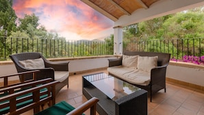 A balcony with wicker furniture, a glass table, and a view of trees and mountains. - Villa 'Es Galliner' with Private Pool, Private Terrace and Wi-Fi (Illes Balears)