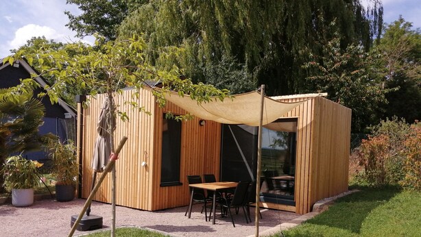 Een houten constructie met een tafel, stoelen en een overkapping, met uitzicht op het omliggende groen.