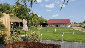 Een houten bankje in een grasrijk gebied met een omheind veld, een gebouw met een rood dak en een houten constructie op de achtergrond.