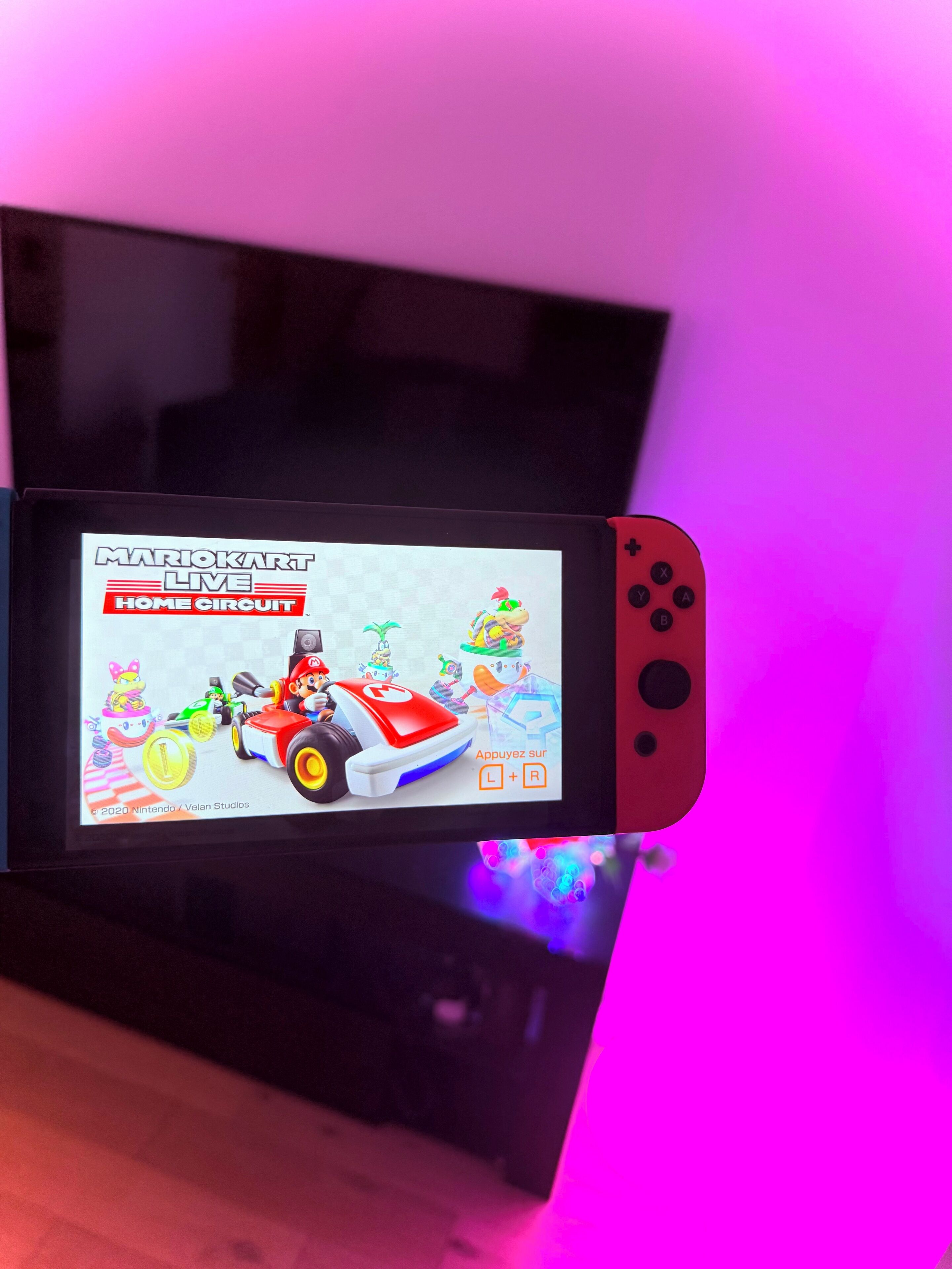 En bärbar spelkonsol som visar ett Mario Kart-spel med ett färgglatt gränssnitt och karaktärer.