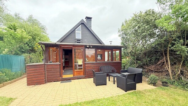 A wooden cabin with a sloped roof, a patio with outdoor furniture, and a garden area.