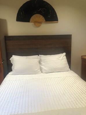 A bed with white bedding, a dark headboard, and a wall-mounted fan above it.