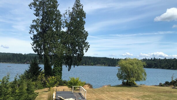 Una terraza con una silla de descanso y una pequeña mesa, con vistas a un lago que tiene un muelle y un bote.