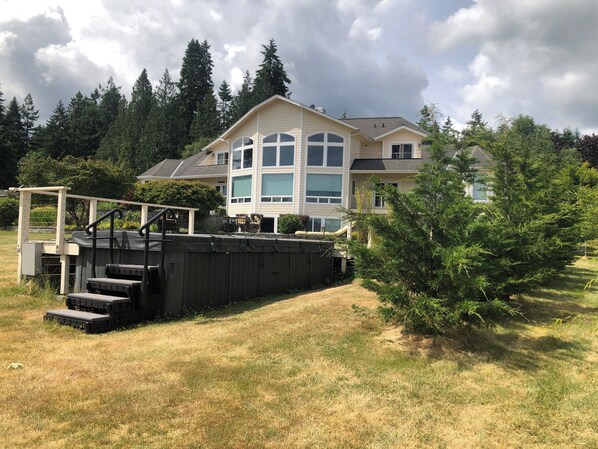 A two-story house with a large deck and a small tree in the yard.