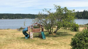 Un parque infantil con tobogán y zona de escalada cerca de un lago.