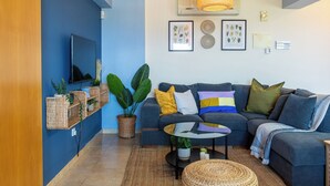 A modern living room with a blue accent wall, a grey sofa, a coffee table, and a large woven basket. - Bayview 2-BR Apartment in Larnaca (Larnaca)
