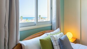 A hotel room with a bed, a bedside lamp, and a window with a view of the beach and ocean. - Bayview 2-BR Apartment in Larnaca (Larnaca)