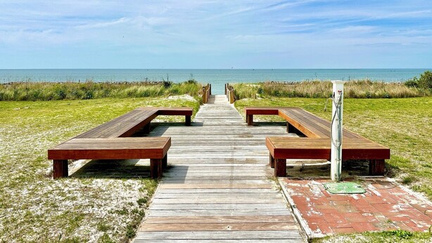 A wooden boardwalk leading to beachside picnic tables with benches.
