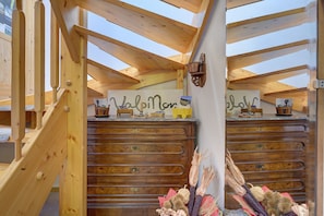 Una scala in legno conduce a una camera da letto mansardata con finestra a lucernario, un comò in legno e un lampadario a parete.