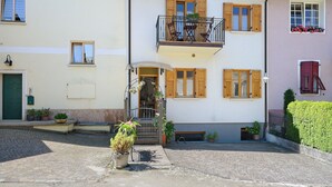 Ein zweistöckiges Gebäude mit einem Balkon, Topfpflanzen und einem Kopfsteinpflasterhof.