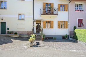 Un edificio a due piani con un balcone, piante in vaso e un cortile in pietra.