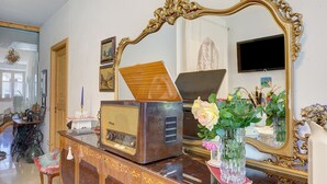Ein altes Radio auf einer Holzkommode, ein Spiegel mit aufwendiger Rahmung und eine Vase mit Blumen.