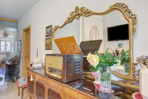 Una radio d'epoca su un mobile in legno, uno specchio con cornice decorata e un vaso con fiori.