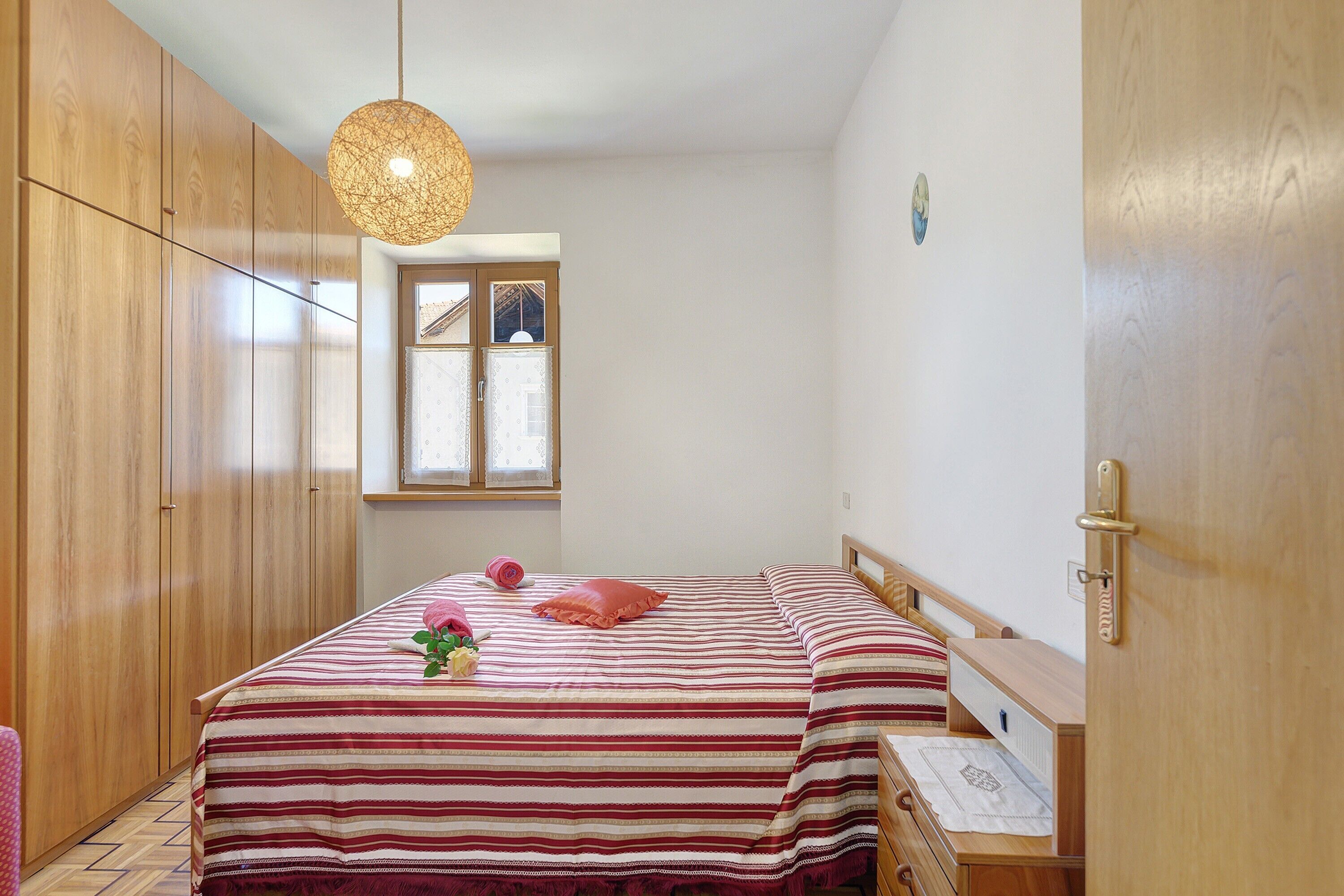 A bedroom with a bed, wooden wardrobe, and a window.