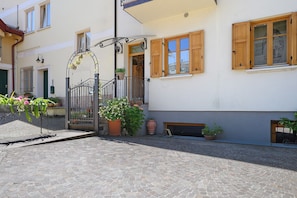 A courtyard with a cobblestone floor, a metal gate, potted plants, and a building with wooden shutters and a balcony.