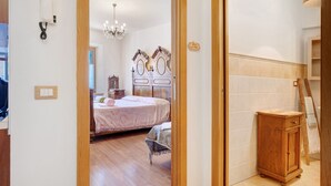A bedroom with a bed, a wooden cabinet, a chandelier, and a door leading to another room. - Apartment 'Odorizzi Dolomiti Di Brenta' with Mountain View, Shared Garden and Balcony (Tassullo)